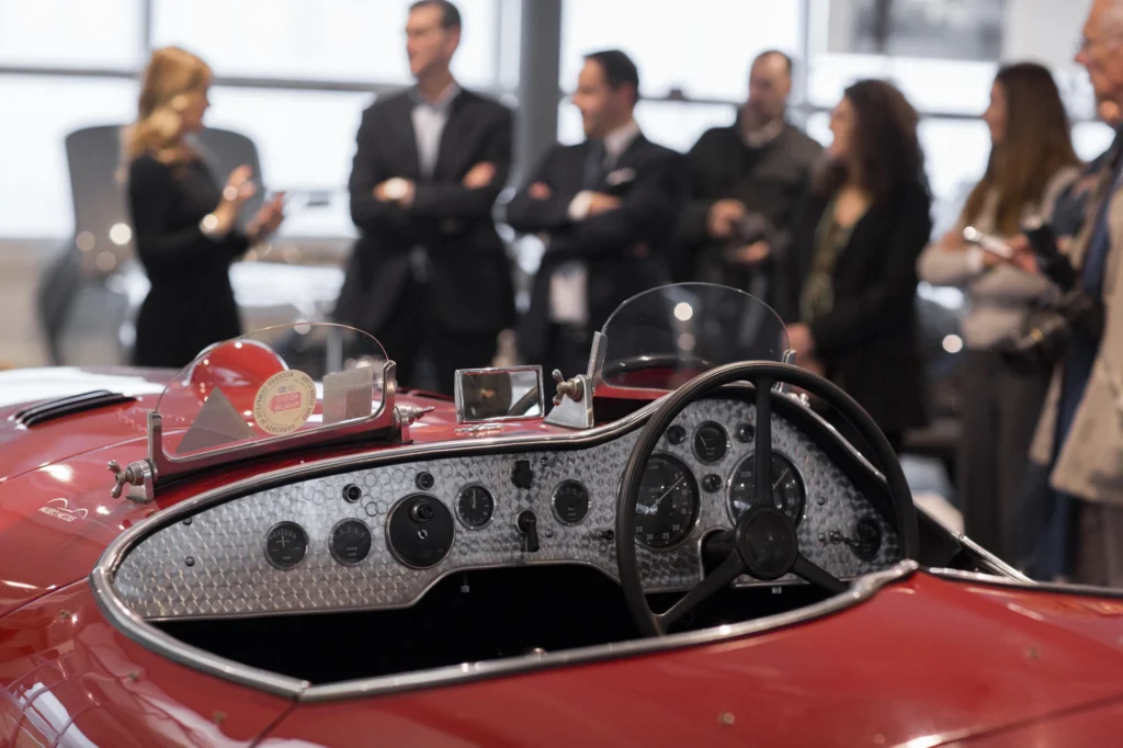 Nell'immagine, un primo piano di un'auto d'epoca, con alcune persone in piedi sullo sfondo